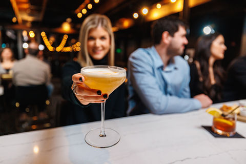 Women holding out drink towards camera
