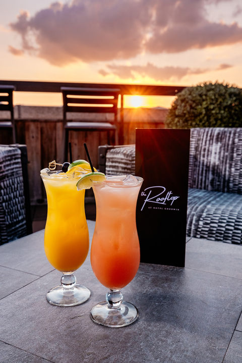 Two cocktails sitting on outdoor table with sun setting in background