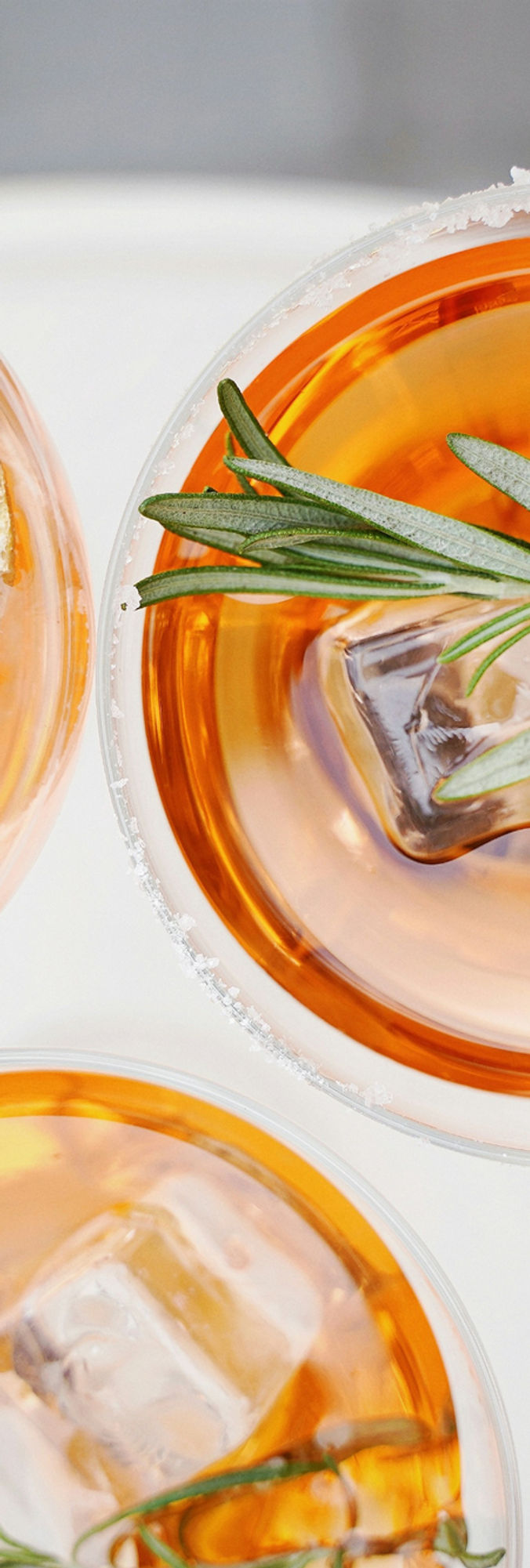 three glasses of orange liquid with ice and herbs
