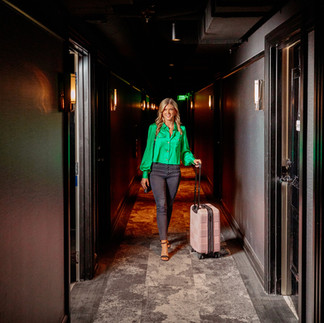 woman in green shirt walking down dark hallway with suitcase