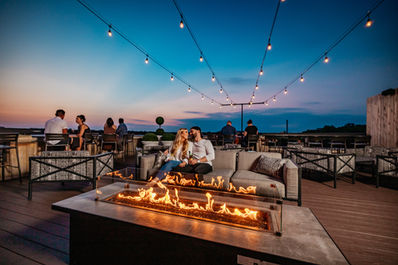 Couple sitting next to outdoor fire pit with sunset in back.