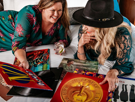 Two woman sitting on bed surrounded by record albums.