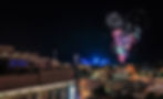 drone photo of fireworks in the distance with people watching from The Rooftop