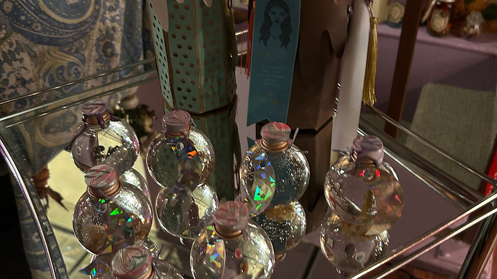 Decorative paper candles and shiny glass ornaments on a silver trolley. Background features a paisley cushion and vintage-style sign.