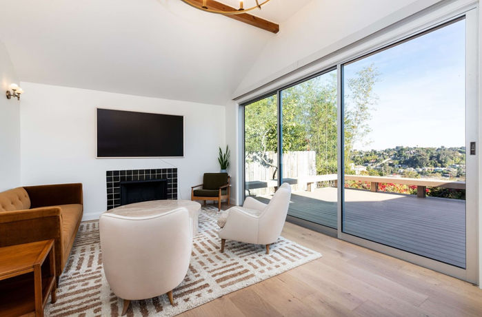 A beautiful, bright living room with a modern fireplace, opening up with big glass doors towards a terrace with an LA view and blue sky.
