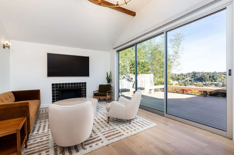A beautiful, bright living room with a modern fireplace, opening up with big glass doors towards a terrace with an LA view and blue sky.