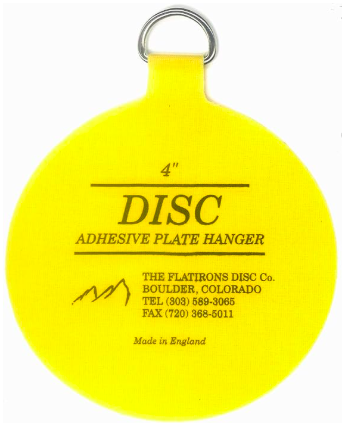 A yellow circular adhesive disc with a metal loop, used to mount plates invisibly for a seamless wall display.