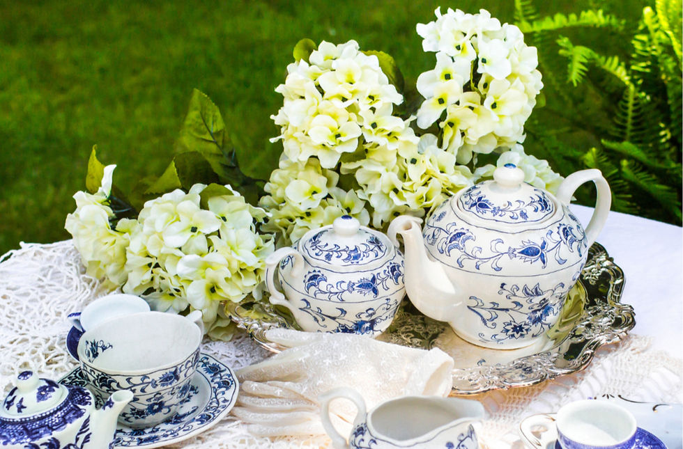 A beautifully arranged white table adorned with blue china, white hydrangeas, and various teapots and cups, creating a classic and inviting tea setting.