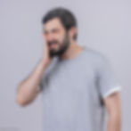 Man in a gray t-shirt holds his cheek, eyes closed in pain against a light gray background, conveying pain from dry socket.