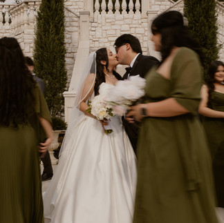 Bride and groom share their first kiss while wedding guests walk past during an outdoor ceremony in Dallas, captured in a candid documentary style.