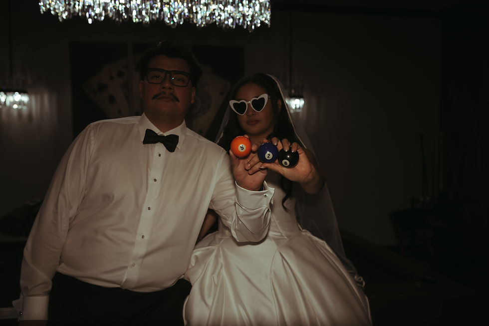 Bride and groom posing with billiard balls and heart-shaped sunglasses during their wedding reception, photographed with a fun editorial style.