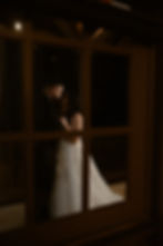 Bride and groom share an intimate moment through a window at their December wedding, captured with warm, cinematic lighting.