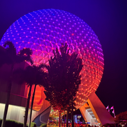 View of Spaceship Earth at night with purple, red, and orange lights.