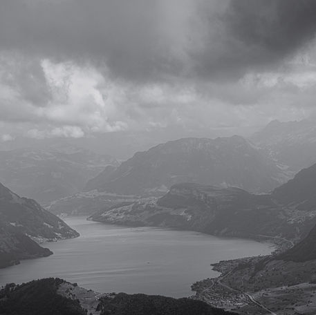 Rechts und Links des See ragen Berge empor. Darüber ein bedeckter Himmel