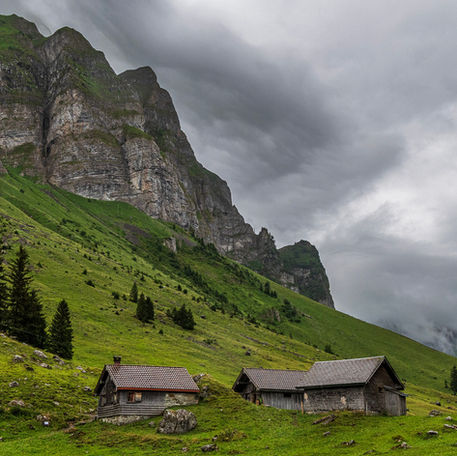 Regenwolken liegen über den Alp mit den Häusern und der Felswand