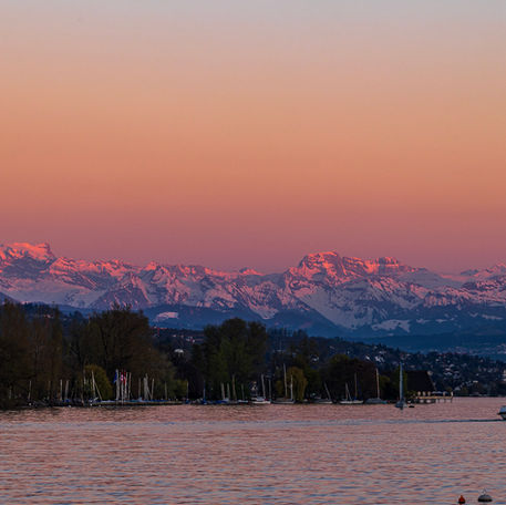 Die Berge und der Himmel haben sich rot verfärbt. Davor fährt ein Passagierschiff über den See