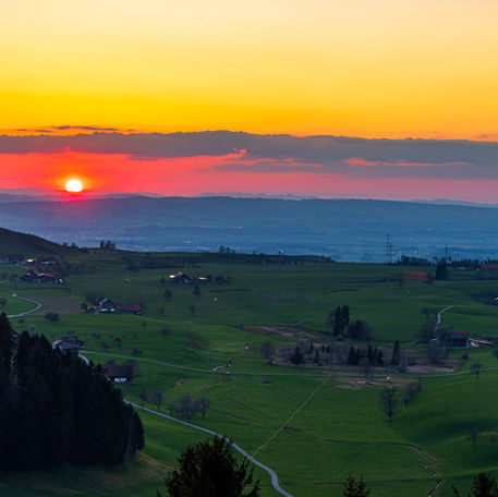 Sonnenuntergang mit Wolken. In der Landschaft stehen verteilt Häuser
