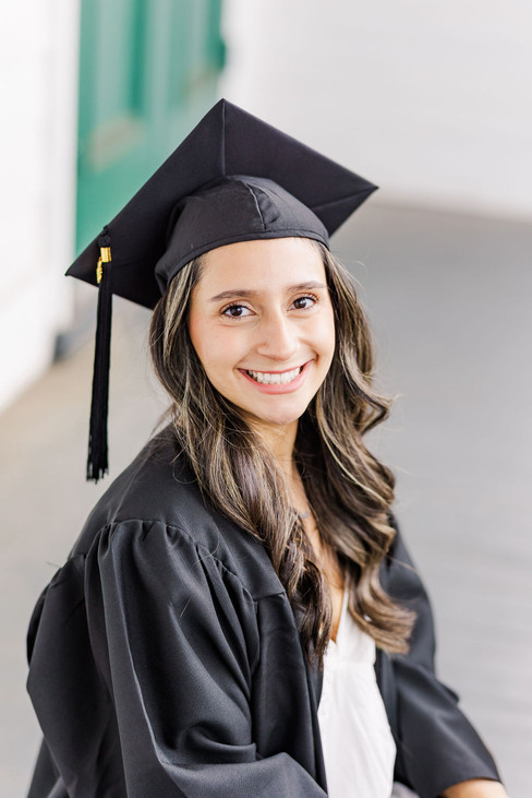 5. Senior portrait in cap and gown smiling near white wall
