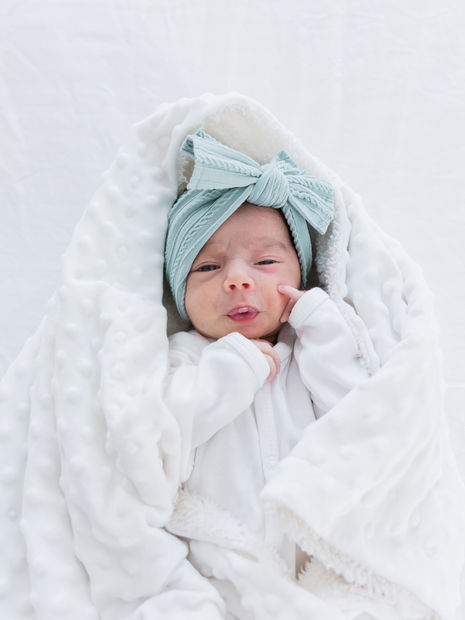 Newborn baby wrapped in a cozy white blanket with a teal bow.