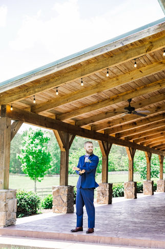 4. Groom standing under wooden arbor at wedding venue