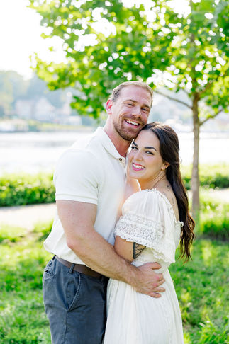 Smiling couple hugging and looking at the camera during their gender reveal session by a river in Northern Virginia.