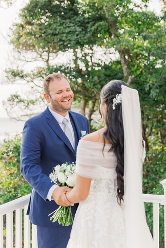 Groom beams with happiness as he sees his bride for the first time during their coastal wedding first look.
