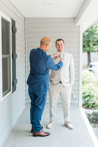 9. Groomsmen helping groom adjust his suit on an airy porch at The Boathouse at Sunday Park.