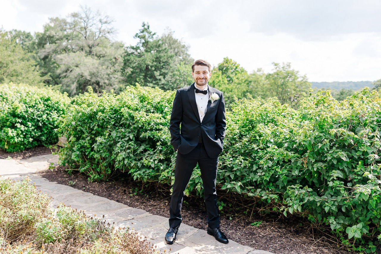 Groom in a black tuxedo standing confidently in a green outdoor space in Richmond, VA.