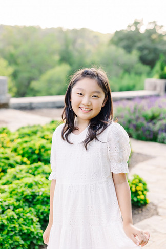 Candid smiling portrait of a young girl in a floral setting, photographed by Richmond Photographer Munhoz Photography.