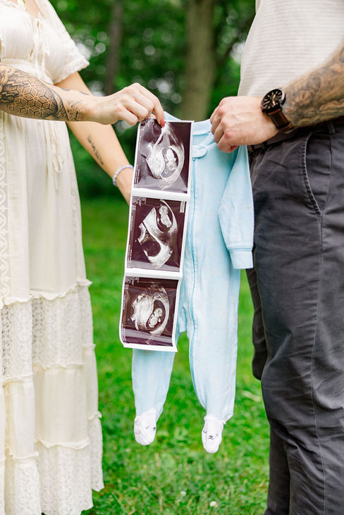 Close-up of couple holding baby’s ultrasound photos and soft blue onesie — detail from Northern Virginia gender reveal photoshoot.
