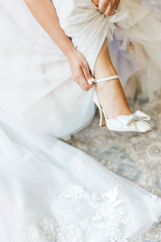 9. Detail photo of the bride putting on delicate white bridal heels.