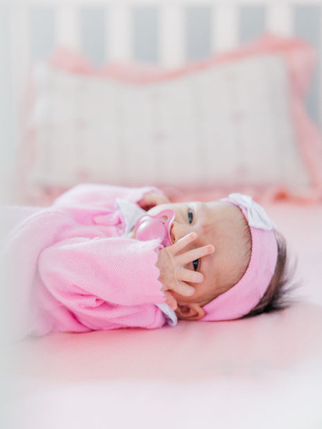 Newborn baby girl in a pink outfit lying on a soft blanket.