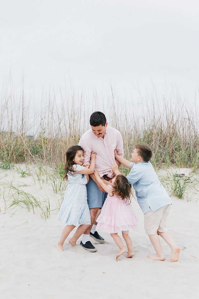 Father happily swinging two daughters around on the beach, laughter on their faces.