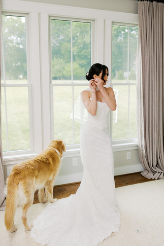 16. Bride adjusting earrings with her golden retriever nearby during wedding morning portraits