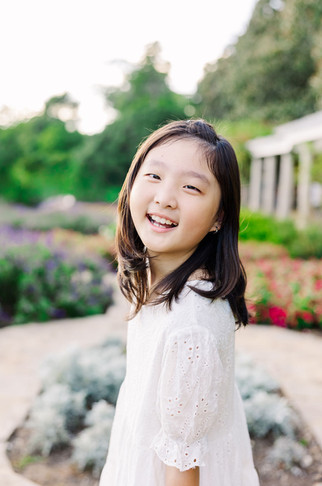 Smiling girl in white lace dress with Maymont’s pergola garden in the background.
