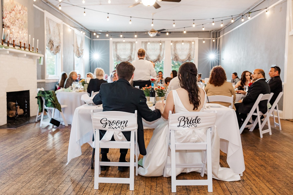 Bride and groom seated at a sweetheart table with “Groom” and “Bride” chair signs at The Schoolhouse at Hawthorne in Richmond, VA.