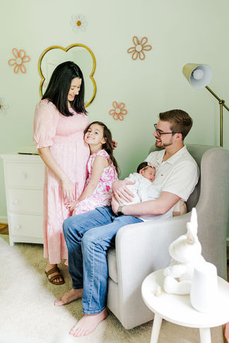 1️⃣6️⃣ Family of four gathered together in nursery chair with newborn.