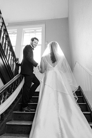 Groom looking back and smiling as he walks up the stairs with the bride at The Schoolhouse at Hawthorne in Richmond, VA.
