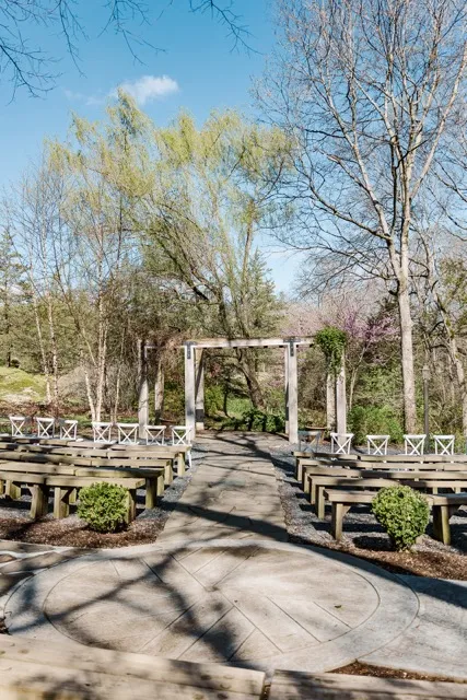 	1.	Outdoor wedding ceremony space at The Mill at Fine Creek, featuring wooden benches and a rustic wooden arbor surrounded by trees.