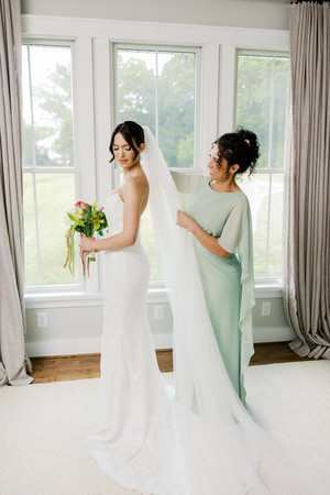 21. Bride holding bouquet while bridesmaid helps with final wedding dress details