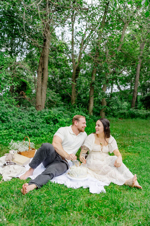 Expecting couple sitting on picnic blanket under trees, smiling during their Northern Virginia gender reveal session.