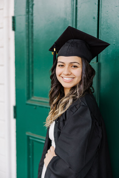 7. Senior smiling in cap and gown in front of green door