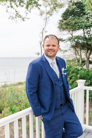 A candid shot of the groom gazing off in thought, dressed in a navy suit with a white boutonniere, ready for his wedding.