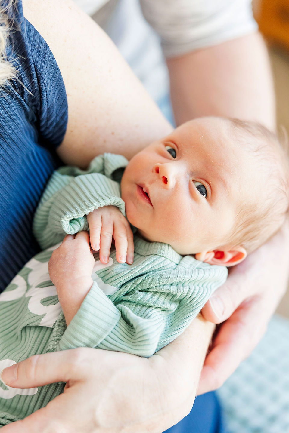 Close-up of a tiny newborn baby, snuggled in mother’s arms in a softly lit nursery in Richmond, Virginia.