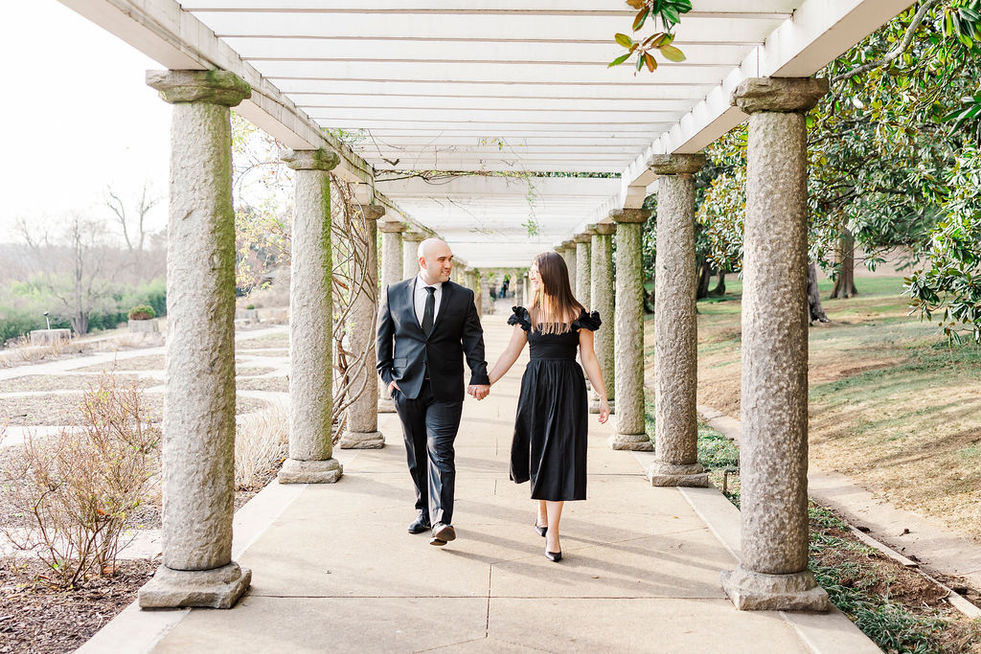 Engaged couple walking under the Maymont Park pergola.