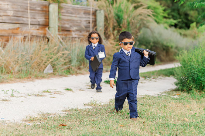 Adorable ring bearers in matching navy suits and sunglasses confidently walk down the aisle at a Virginia Beach wedding.