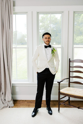 4. Groom standing by bright windows in a white tuxedo jacket before his private residence wedding ceremony