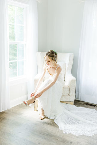 16. Bride putting on shoes in natural light by window