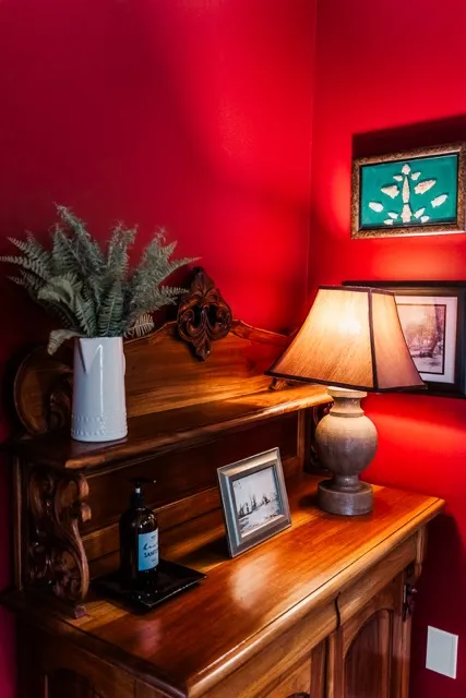	4.	Close-up of a wooden mantel with framed photos, a decorative lamp, and floral arrangements against a deep red wall.