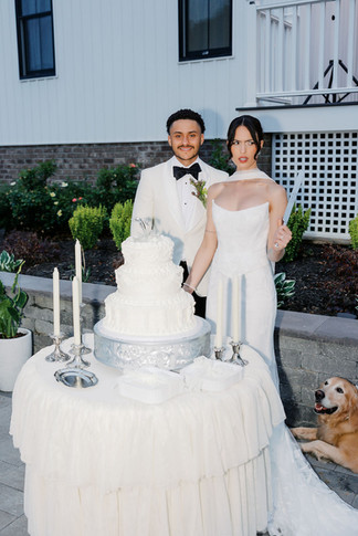 12. Bride and groom standing beside their wedding cake with their golden retriever Fry nearby